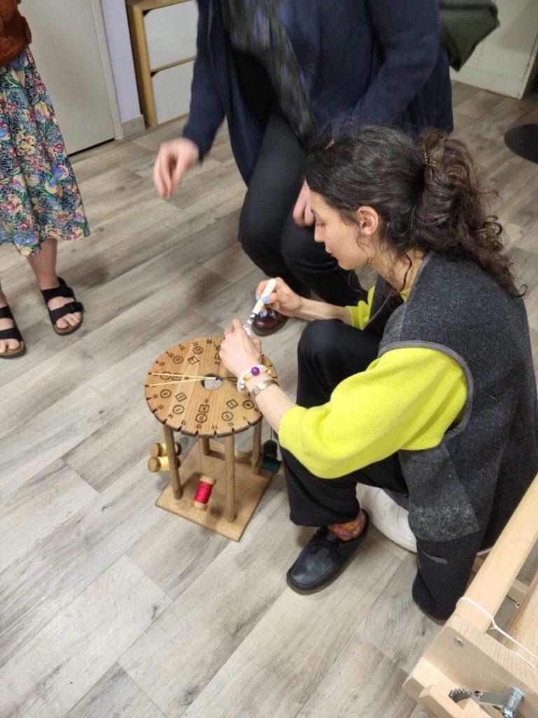 A workshop Kumihimo braiding session in Paris showing participants seated around traditional wooden Marudai looms.